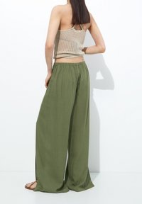 Débardeur beige léger en maille associé à un pantalon large olive à taille élastique avec cordon et fentes latérales.