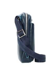 Marineblaue Leder-Crossbody-Tasche mit glatter Textur, ausgestattet mit einem silbernen Reißverschluss, einem verstellbaren Stoffgurt und hellblauen Akzenten.