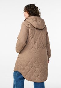 Ruskea tikattu pitkä takki hupulla, jossa aaltoilevat kuviot, joustavat hihansuut ja hieman kaartuva helma. Ulkokangas näyttää sileältä.