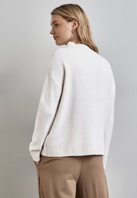Maglione a maglia beige chiaro con orlo e colletto a coste. Presenta spalle ribassate e un tessuto morbido e texturizzato. Design minimalista, senza motivi visibili.