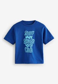 Sininen puuvillapaita, jossa on teksti "Surf Skate Club" vaaleansinisellä värillä sekä aalto- ja skeittigrafiikoita, klassinen pyöreä kaulus ja lyhyet hihat.