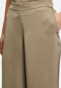 Beżowe spodnie typu wide-leg, wykonane z gładkiego, lekkiego materiału. Cechują się wysokim stanem oraz bocznymi kieszeniami, z delikatnymi plisowaniami.