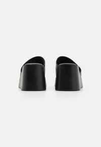 Mules à plateforme noires en matériau lisse, avec un dessus incurvé et un épais talon bloc, conçues avec des lignes épurées et des accents minimalistes.
