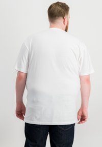 Weißes T-Shirt mit kurzen Ärmeln und rundem Halsausschnitt, aus weichem Stoff gefertigt. Die Rückansicht zeigt eine glatte Textur und einen lockeren Schnitt. Kombiniert mit dunklen Jeans.