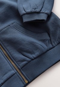 Sweatshirt à fermeture éclair bleu foncé avec poignets et ourlet côtelés, comprenant une grande poche avant et une fermeture éclair métallique sur l'ouverture avant.