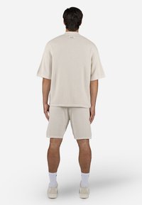 Beige cotton ribbed short-sleeve top and matching shorts. Both have a relaxed fit and visible texture. White sneakers and socks complete the look.