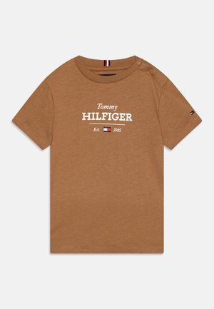Ruskea lyhythihainen taaperoiden paita, jossa teksti "Tommy Hilfiger Est. 1985" sekä pieni logo hihoissa ja rinnassa, nappi olkapäällä.