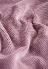 Weicher rosa Cordstoff mit feiner gerippter Textur, der sich in sanften Falten drapieren lässt und das plüschige Material sowie eine warme, sanfte Farbe betont.