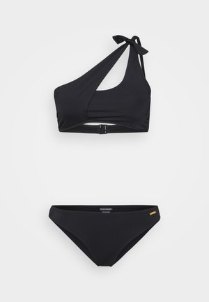 Must mustriin komplekt, kus on ühekohaline ülaserk, millel on ees lõikega ja sõlm, ning klassikalised madala lõikega aluspüksid, millel on diskreetne logodetail.