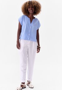 Niebiesko-biała, paskowana bluzka z krótkim rękawem, wycięciem w kształcie litery V i guzikami z przodu, w komplecie z białymi spodniami i jasnymi sandałami. Gładka tekstura materiału.