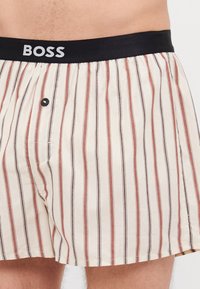 Shorts de détente en coton rayés beige, rouge et bleu marine. Dotés d'une taille élastique noire avec le logo "BOSS" et d'un détail de bouton à l'avant.