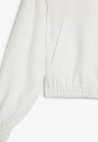 Hvid cropped jakke med lange, puffede ærmer, elastiske manchetter og en sidelomme. Glat tekstur med et minimalistisk design.
