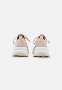 Zapatillas deportivas de color beige claro con parte superior de punto texturizado, suela blanca plana y contrafuerte moldeado en el talón. Cordones anudados y lazos planos en el talón.