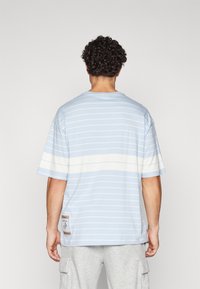 Lyseblå stribet t-shirt, korte ærmer, rund hals, med hvide vandrette striber og et mærkepatch på nederste venstre side.