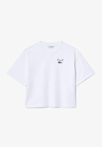 Balta medvilnė trumpomis rankovėmis marškinėliai su žaliu siuvinėtu krokodilo logotipu ir "Lacoste" tekstu kairėje krūtinės pusėje. Laisvas, sutrumpintas dizainas.