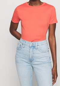 Coral fitted t-shirt with short sleeves, round neckline, paired with light blue high-waisted jeans. Cotton material, smooth texture.