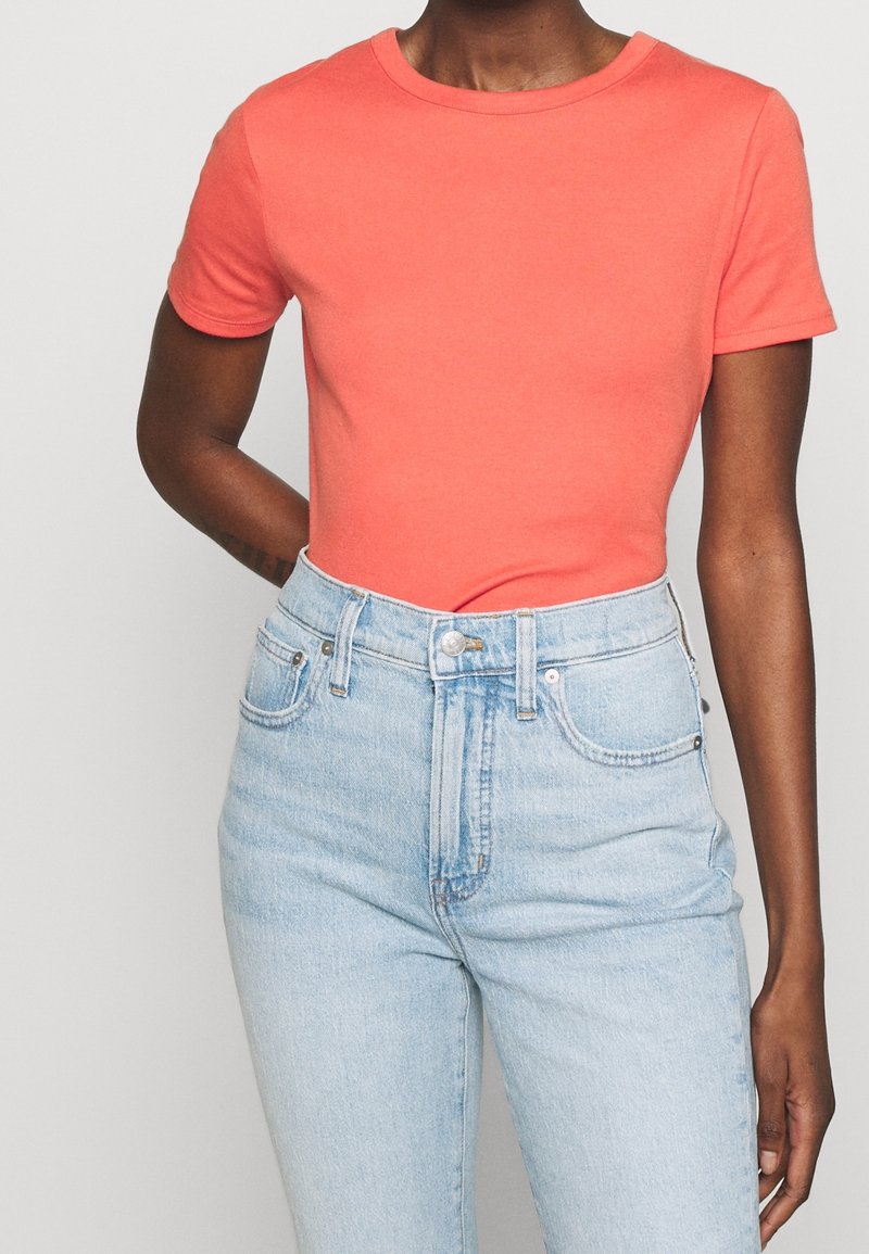 Coral fitted t-shirt with short sleeves, round neckline, paired with light blue high-waisted jeans. Cotton material, smooth texture.