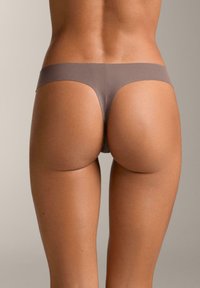 Nahtloser String aus hellbraunem Stoff mit minimalistischem Design, niedrigem Bund und glatter Textur.