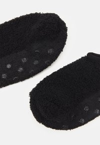 Calcetines de forro polar negros con una superficie texturizada, que cuentan con antideslizantes de goma en las suelas para mayor agarre y un puño elástico ceñido en la parte superior.