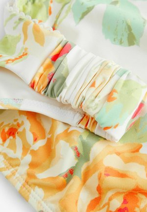 Virágmintás vászon lágy sárga, narancs, zöld és korall árnyalatokban. Gyűrt textúrával és csipkés élekkel rendelkezik, amely réteges megjelenést kölcsönöz.