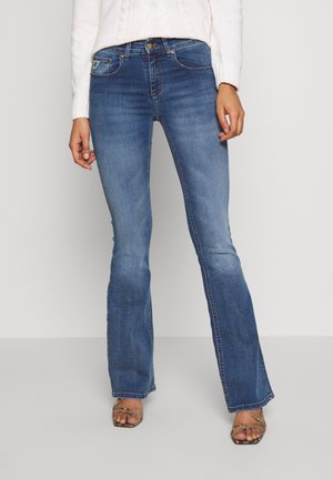 Dark blue flared jeans with a smooth denim texture, traditional five-pocket style, and slight fading on the thighs, paired with strappy sandals.