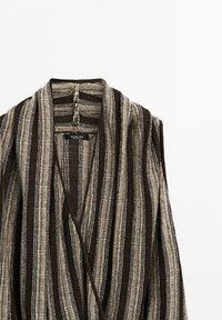 Gestreepte bruine en beige textuurgebreide cardigan met open voorkant en sjaalkraag, plat gelegd op een wit oppervlak.