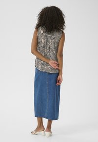 Ærmeløs top med en beige baggrund, der har sorte bladmønstre, parret med en lang blå denimnederdel og hvide hælede sandaler.