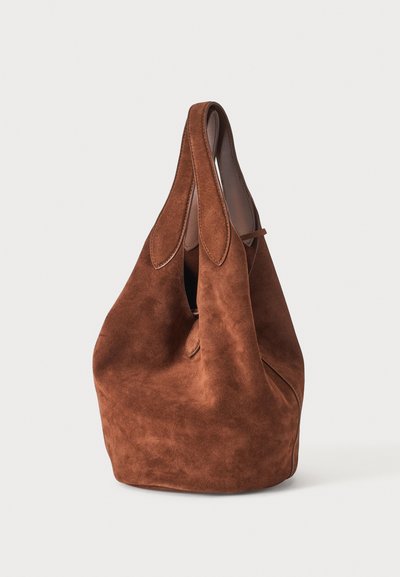 Sac à main en daim marron avec une forme souple et décontractée et des poignées intégrées sur un fond clair uni.