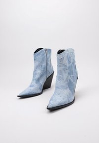 Botas de tobillo de mezclilla azul con punta afilada, tacón alto en cuña y cierre de cremallera, con una superficie texturizada y detalles de costura.