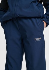 Marinblå sportset som har ribbad struktur, elastisk midja och sidofickor. Logotypen "hummel" visas i silver på byxorna.