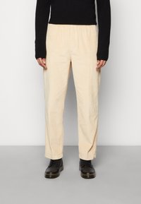 Ljusbeige kordflosbyxor med avslappnad passform, utrustade med elastisk midja och raka ben, tillsammans med svarta snörskor.