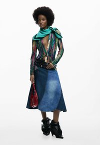 Bluza tricotată multicolor cu decolteu în V, asortată cu o fustă A-line din denim, geantă roșie și cizme scurte negre.