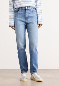 Lichtblauwe denim jeans met een hoge taille, rechte pijpen en minimale slijtage, gecombineerd met een gestreepte lange mouw shirt en sneakers.
