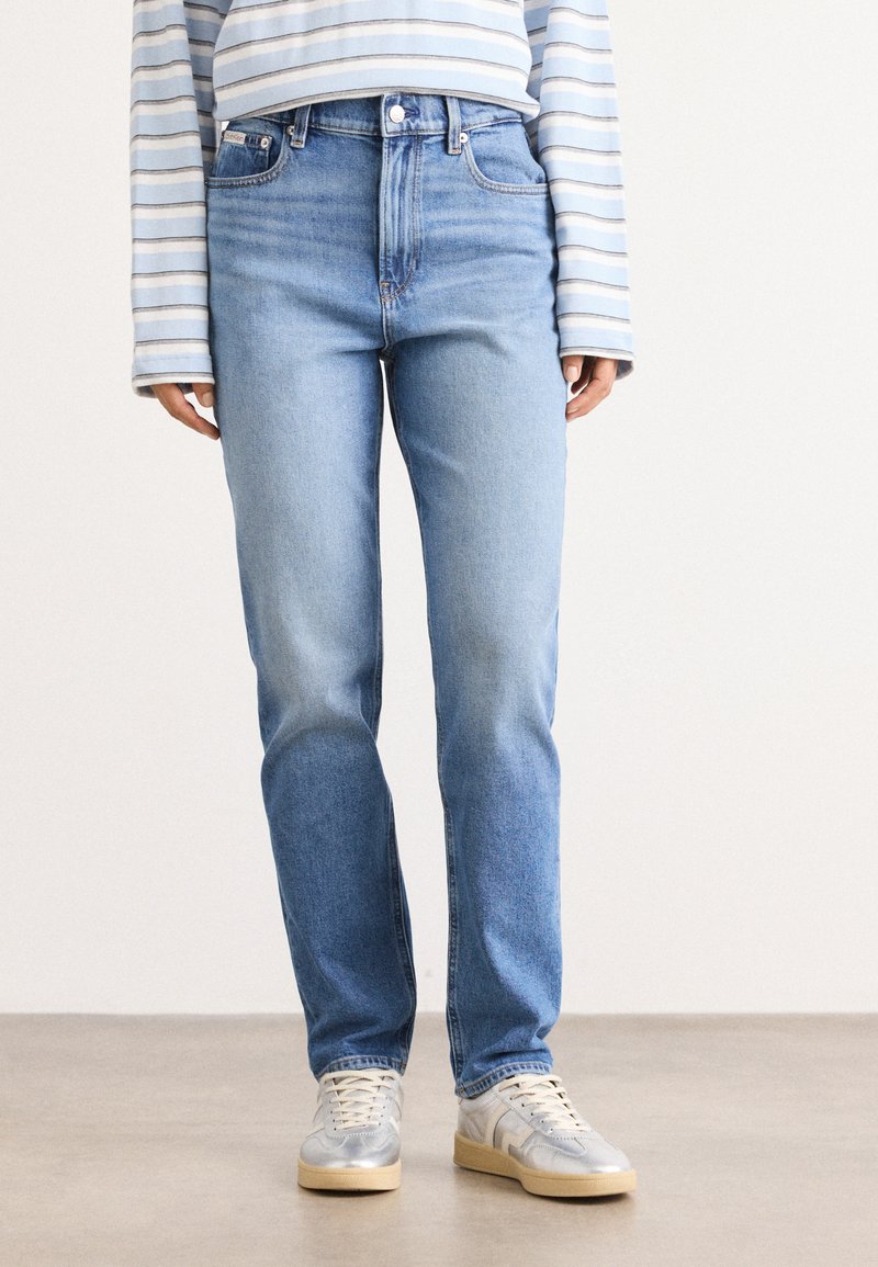 Lichtblauwe denim jeans met een hoge taille, rechte pijpen en minimale slijtage, gecombineerd met een gestreepte lange mouw shirt en sneakers.