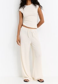 Completo a due pezzi a coste di un beige chiaro, composto da una maglietta aderente a maniche corte e pantaloni a gamba larga con vita elasticizzata e cordino.