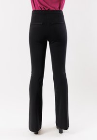 Pantaloni neri a zampa d'elefante con una superficie liscia, dotati di due tasche posteriori e una vita a media altezza. Il tessuto è leggero ed elastico.