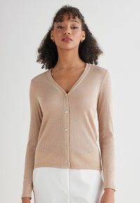 Beżowy kardigan z prążkowanym splotem, z dekoltem w serek, długimi rękawami i zapięciem na guziki. Posiada miękką fakturę i subtelny połysk.