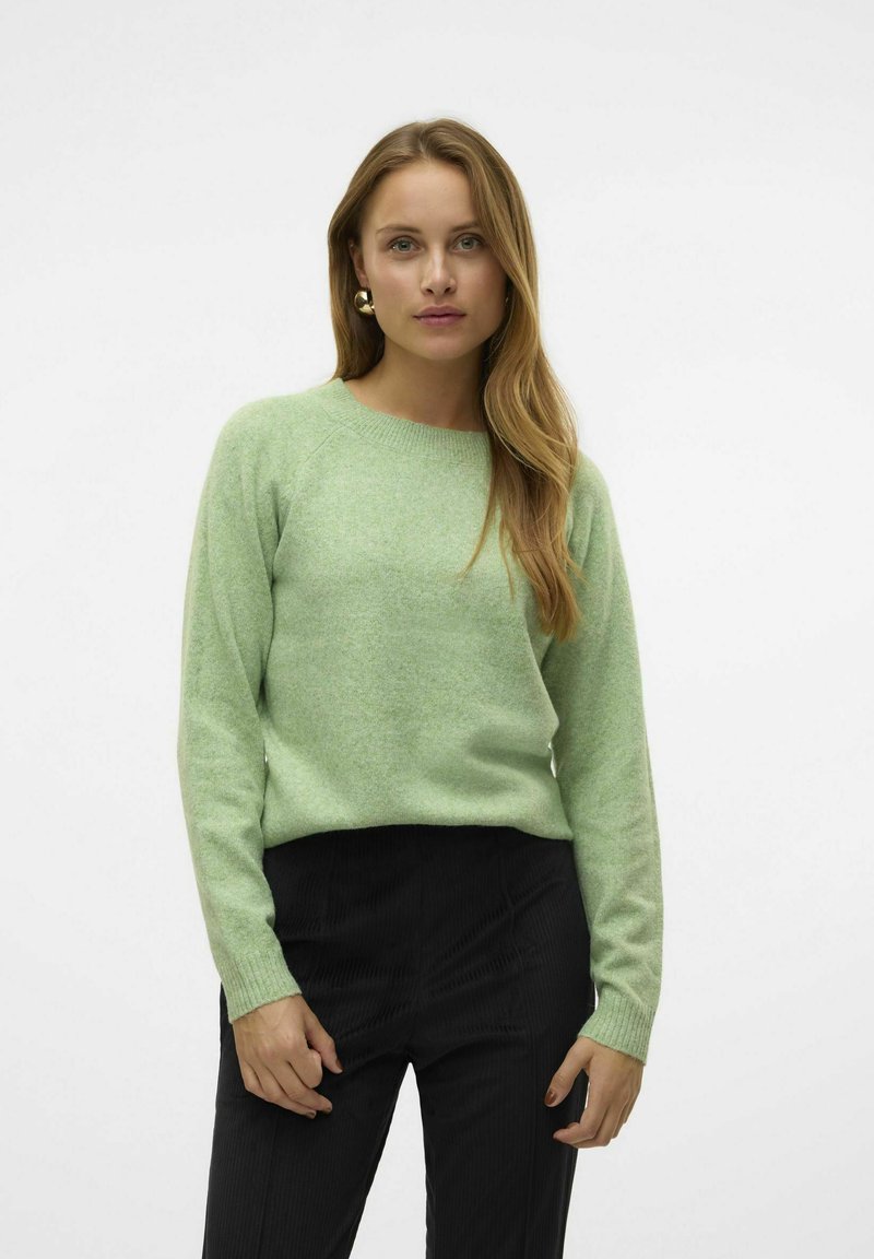 Maglione verde chiaro con collo e polsini a coste, caratterizzato da una texture morbida. Abbinato a pantaloni in velluto a coste neri. Nessun motivo o decorazione.