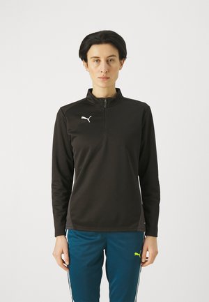 Maglietta nera a mezza zip a maniche lunghe con accenti bianchi del logo, abbinata a pantaloni della tuta blu con strisce laterali bianche e un piccolo logo.
