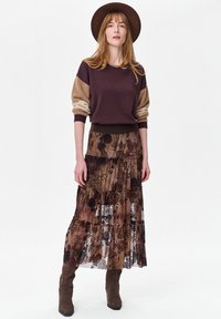 Gebreide trui in donkerpaars met beige accenten, gecombineerd met een gelaagde bruine rok met bloemenpatroon en bruine enkellaarsjes. Voorzien van een hoed met brede rand.