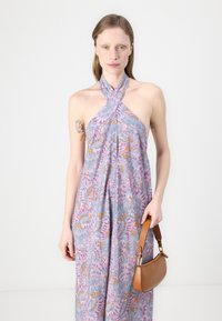Lila gemustertes Halterkleid mit fließendem Design, ausgestattet mit einer Knopfleiste und bunten Akzenten. Ergänzt wird das Outfit durch eine braune Schultertasche.