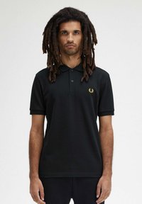 Polo shirt nero a maniche corte, con patta a due bottoni e logo ricamato in oro sul lato sinistro del petto. Tessuto morbido con una vestibilità comoda.