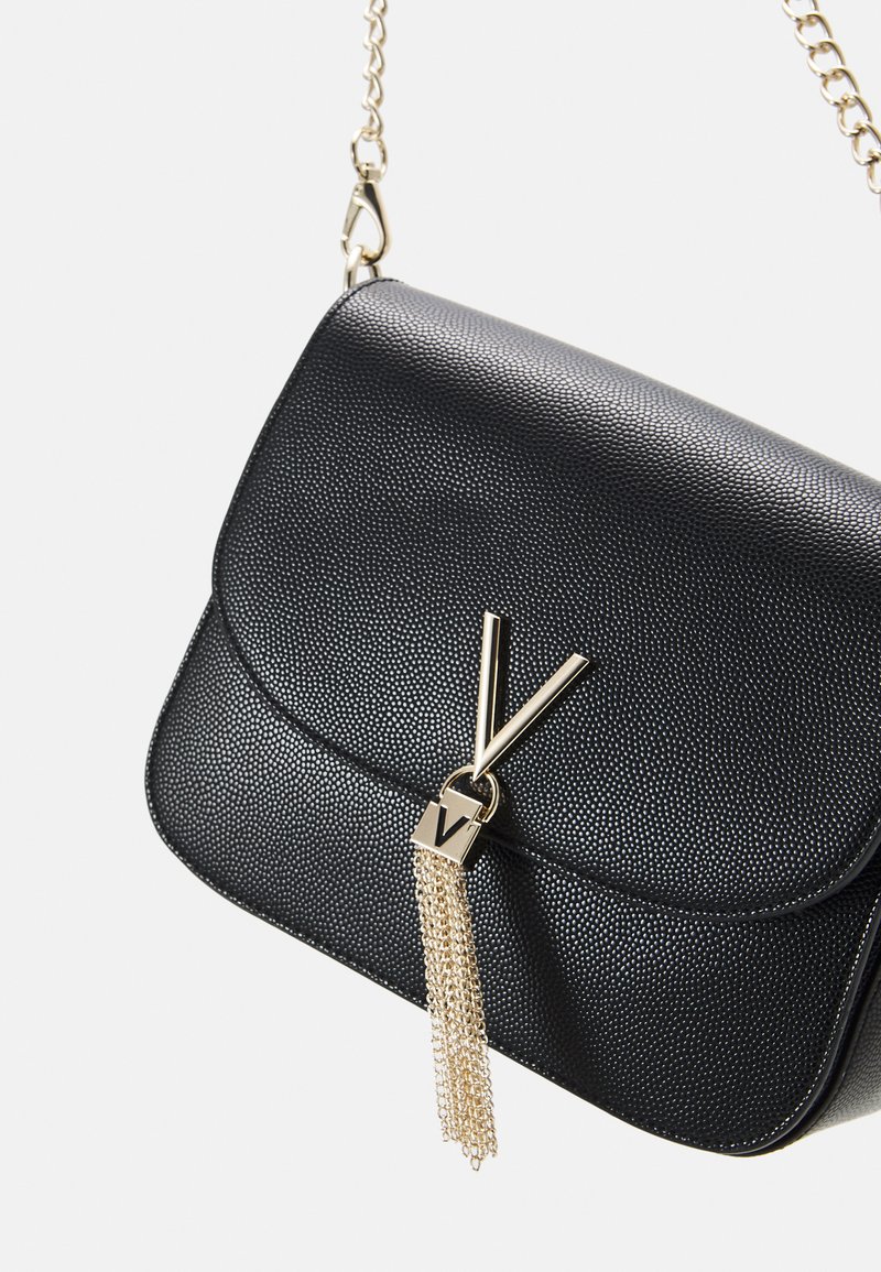 Bolso de mano negro texturizado con una correa de cadena dorada, que presenta un acento metálico en forma de V y un detalle de borla para una decoración adicional.