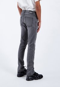 Jeans de mezclilla gris con un corte ajustado, diseño de cinco bolsillos, costuras visibles y una etiqueta de marca en la parte trasera de la cintura, combinados con zapatillas negras.