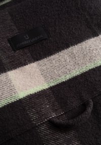 Károvaná tkanina v tmavě šedé a krémové barvě s zelenými akcenty. Obsahuje černou etiketu s nápisem "JOHNNY URBAN." Jemný, texturovaný směsový materiál z vlny.