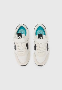 Baskets blanches de sport avec des accents noirs, en matériau mesh et suède, avec des lacets ronds et une semelle intérieure turquoise ornée d'un motif de cercles concentriques.