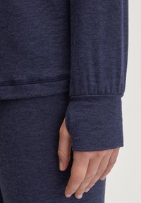 Marineblauwe langermouwtop met een ontspannen pasvorm, zachte textuur en aangesloten manchetten met duimgaten. Zichtbare stikseldetails aan de zoom.