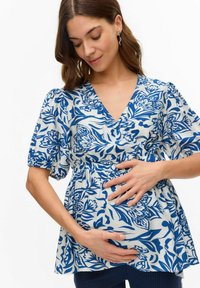 Blus med blommönster i vitt och blått, med v-ringning, korta puffärmar och elastisk midja som draperar över magen.