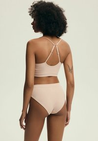 Jasnoróżowy staniczek z prążkowanej tkaniny z regulowanymi ramiączkami i dopasowanym, wysokim dołem. Gładka faktura i minimalistyczny design.