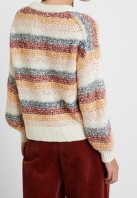 Suéter de punto a rayas multicolores con tonalidades de naranja, crema y azul. Dobladillo y puños acanalados, con un corte relajado y tejido texturizado.